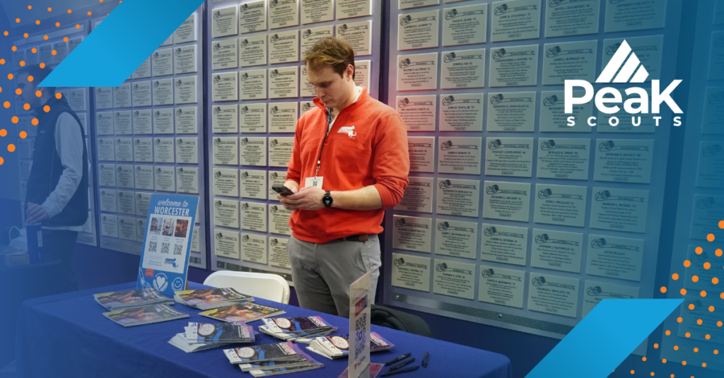 A sports professional at an event booth, reviewing information about resources on his phone in front of a wall of plaques.